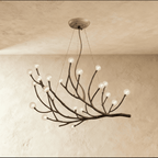 Clérachic branch chandelier in clear glass globes, unlit, its bronze branches spread wide against a plaster wall.