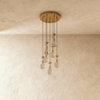 Clérachic chandelier with 7 clear glass teardrops on thin cords from a round brushed gold canopy, switched off, against limewashed plaster