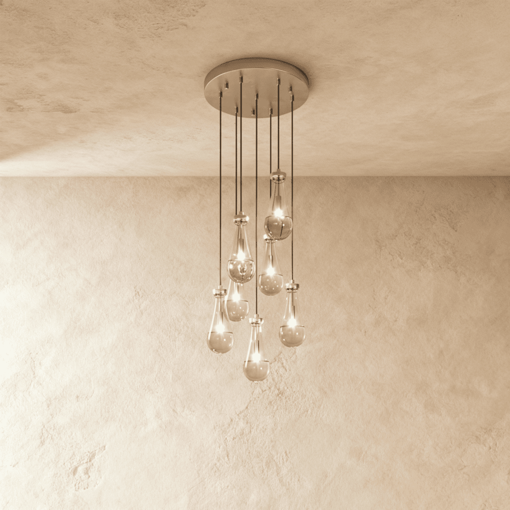 Clérachic chandelier with 7 clear glass teardrops on thin cords from a round satin nickel canopy, glowing warm, against limewashed plaster