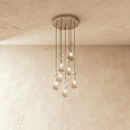Clérachic chandelier with 7 clear glass teardrops on thin cords from a round satin nickel canopy, glowing warm, against limewashed plaster