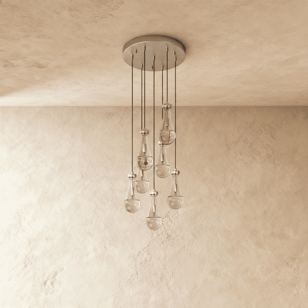 Clérachic chandelier with 7 clear glass teardrops on thin cords from a round satin nickel canopy, switched off, against limewashed plaster