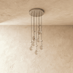 Clérachic chandelier with 7 clear glass teardrops on thin cords from a round satin nickel canopy, switched off, against limewashed plaster