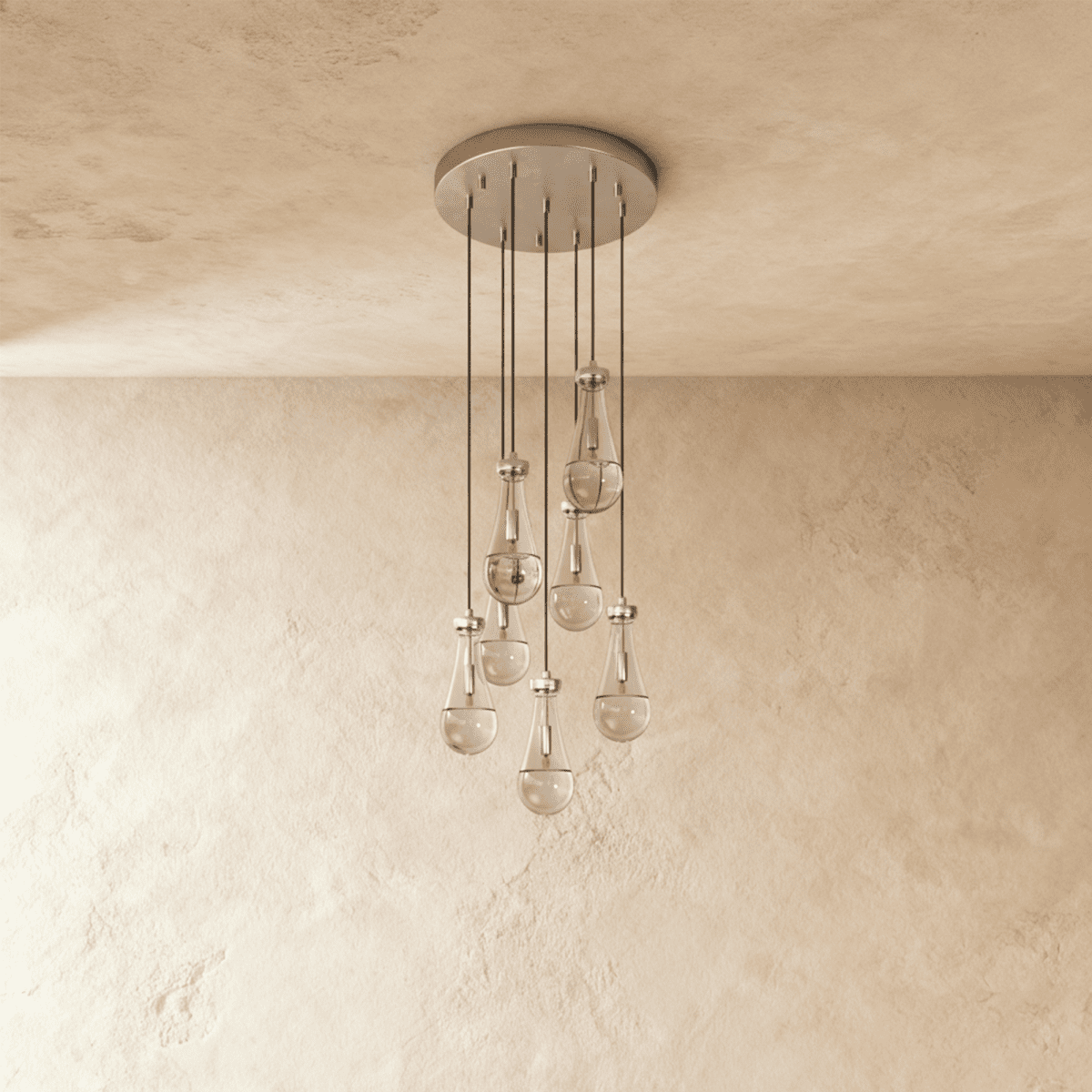 Clérachic chandelier with 7 clear glass teardrops on thin cords from a round satin nickel canopy, switched off, against limewashed plaster