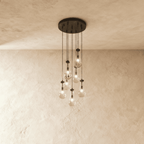Clérachic chandelier with 7 clear glass teardrops on thin cords from a round dark bronze canopy, glowing warm, against limewashed plaster