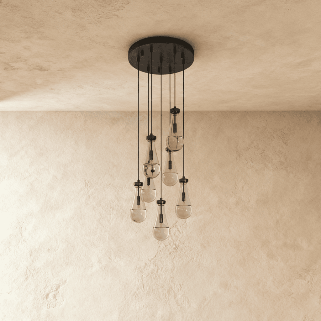 Clérachic chandelier with 7 clear glass teardrops on thin cords from a round dark bronze canopy, switched off, against limewashed plaster