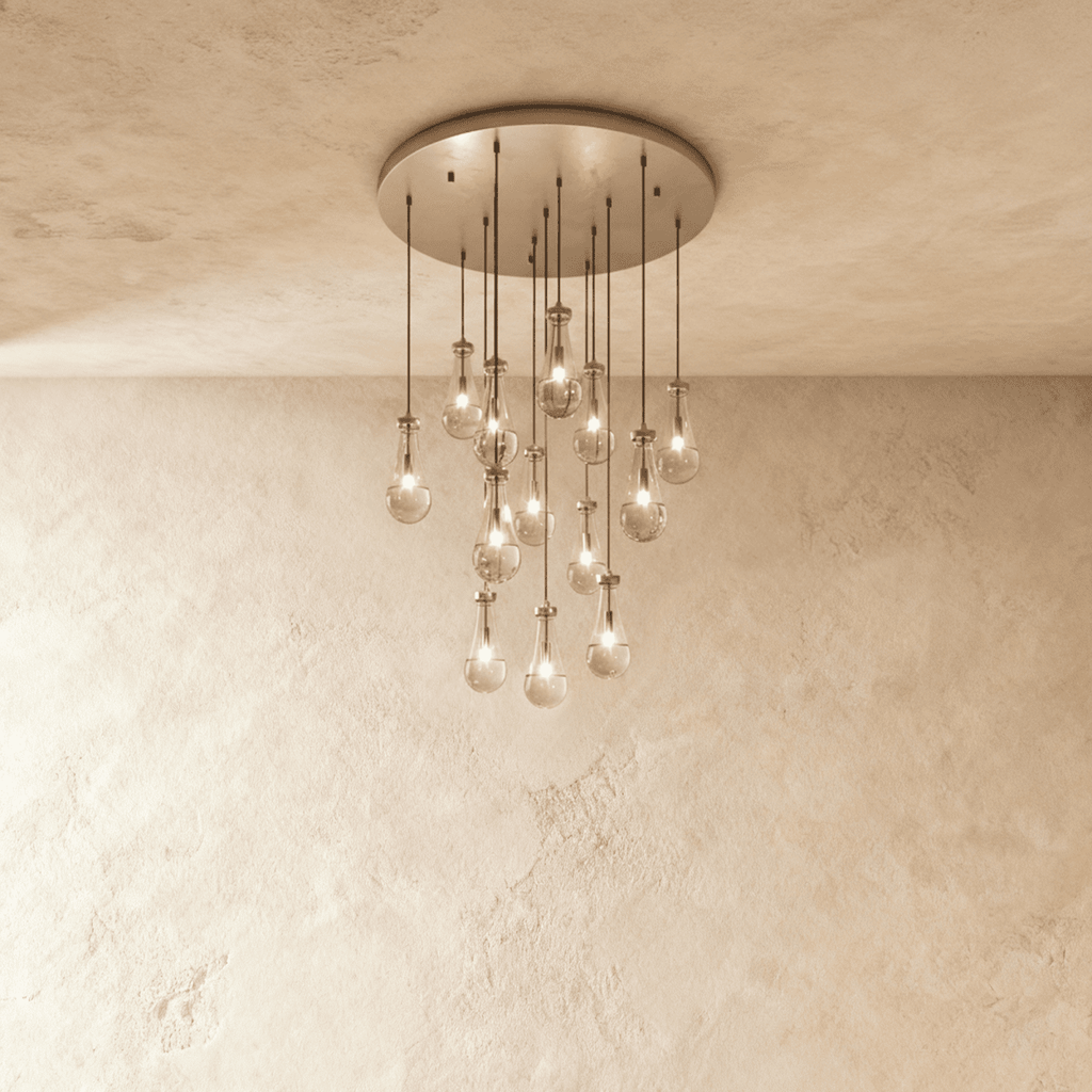 Clérachic chandelier with 13 clear glass teardrops on thin cords from a round satin nickel canopy, glowing warm, against limewashed plaster