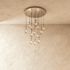 Clérachic chandelier with 13 clear glass teardrops on thin cords from a round satin nickel canopy, glowing warm, against limewashed plaster