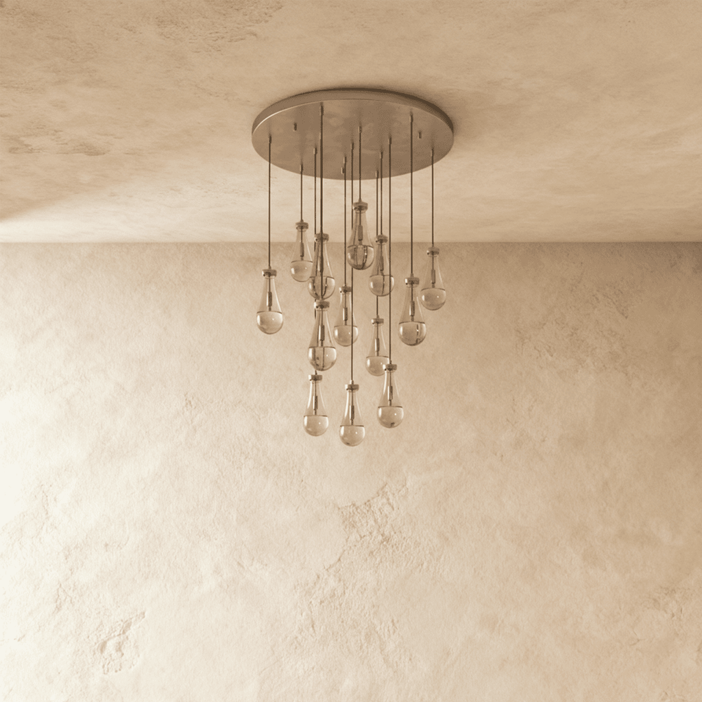 Clérachic chandelier with 13 clear glass teardrops on thin cords from a round satin nickel canopy, switched off, against limewashed plaster