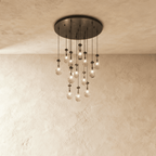 Clérachic chandelier with 13 clear glass teardrops on thin cords from a round dark bronze canopy, glowing warm, against limewashed plaster