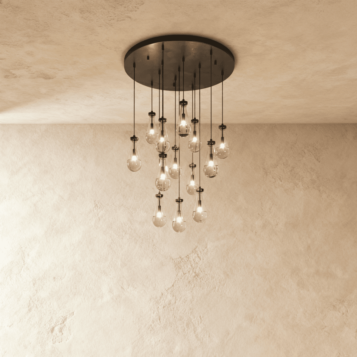 Clérachic chandelier with 13 clear glass teardrops on thin cords from a round dark bronze canopy, glowing warm, against limewashed plaster
