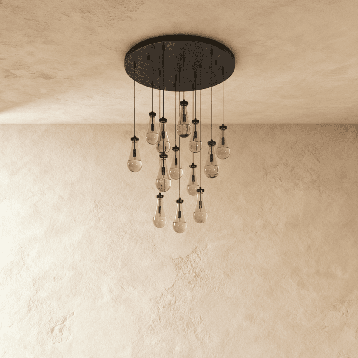 Clérachic chandelier with 13 clear glass teardrops on thin cords from a round dark bronze canopy, switched off, against limewashed plaster