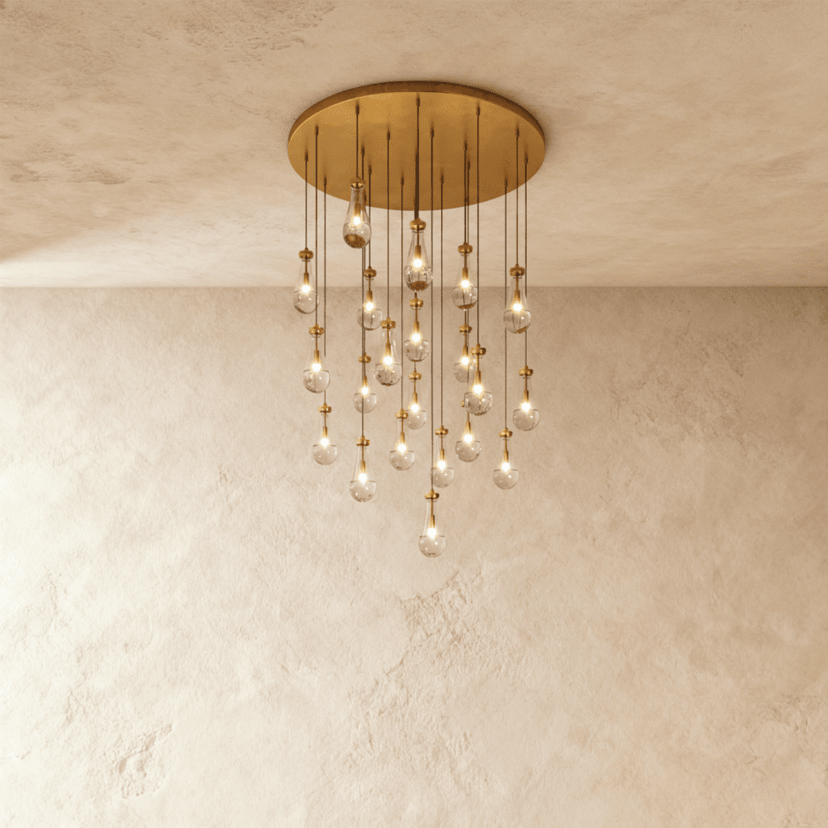 Clérachic chandelier with 21 clear glass teardrops on thin cords from a round brushed gold canopy, glowing warm, against limewashed plaster