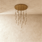 Clérachic chandelier with 21 clear glass teardrops on thin cords from a round brushed gold canopy, switched off, against limewashed plaster