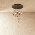 Clérachic chandelier with 21 clear glass teardrops on thin cords from a round dark bronze canopy, glowing warm, against limewashed plaster