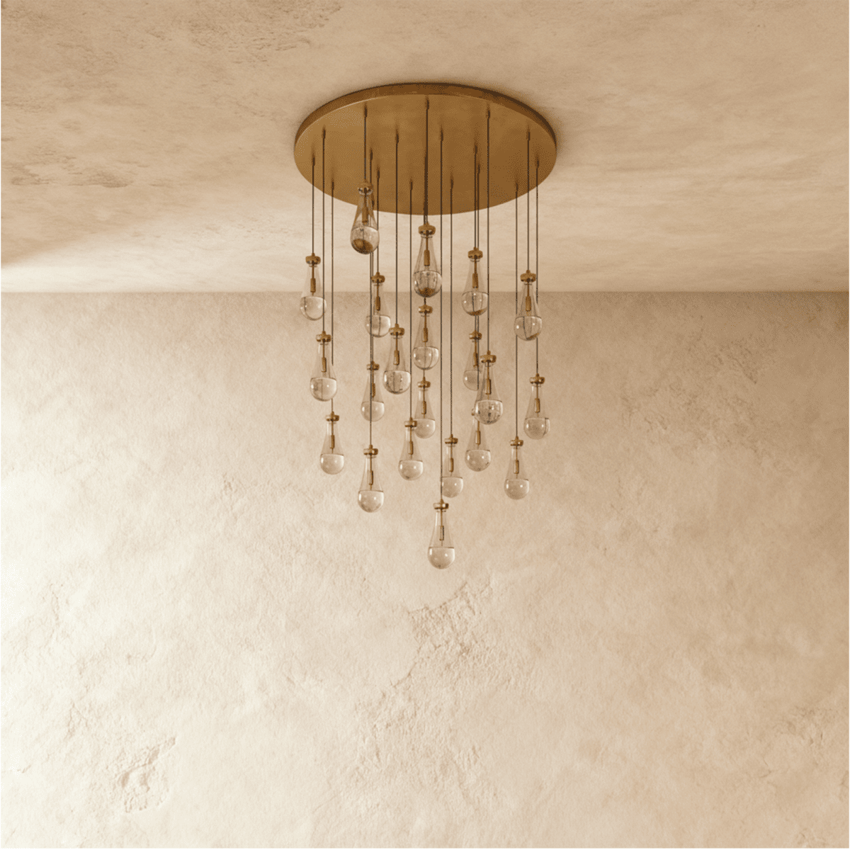 Clérachic chandelier with 21 clear glass teardrops on thin cords from a round brushed gold canopy, switched off, against limewashed plaster