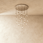 Clérachic chandelier with 21 clear glass teardrops on thin cords from a round satin nickel canopy, glowing warm, against limewashed plaster