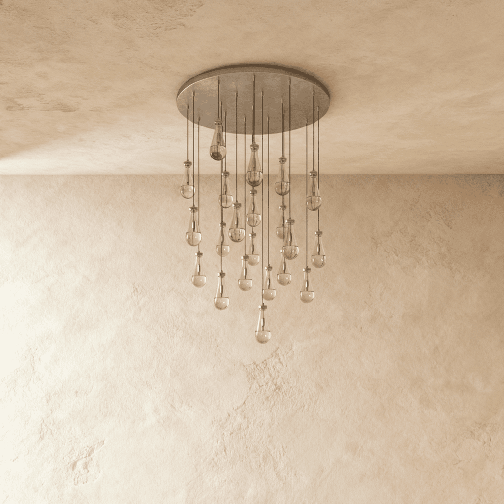 Clérachic chandelier with 21 clear glass teardrops on thin cords from a round satin nickel canopy, switched off, against limewashed plaster