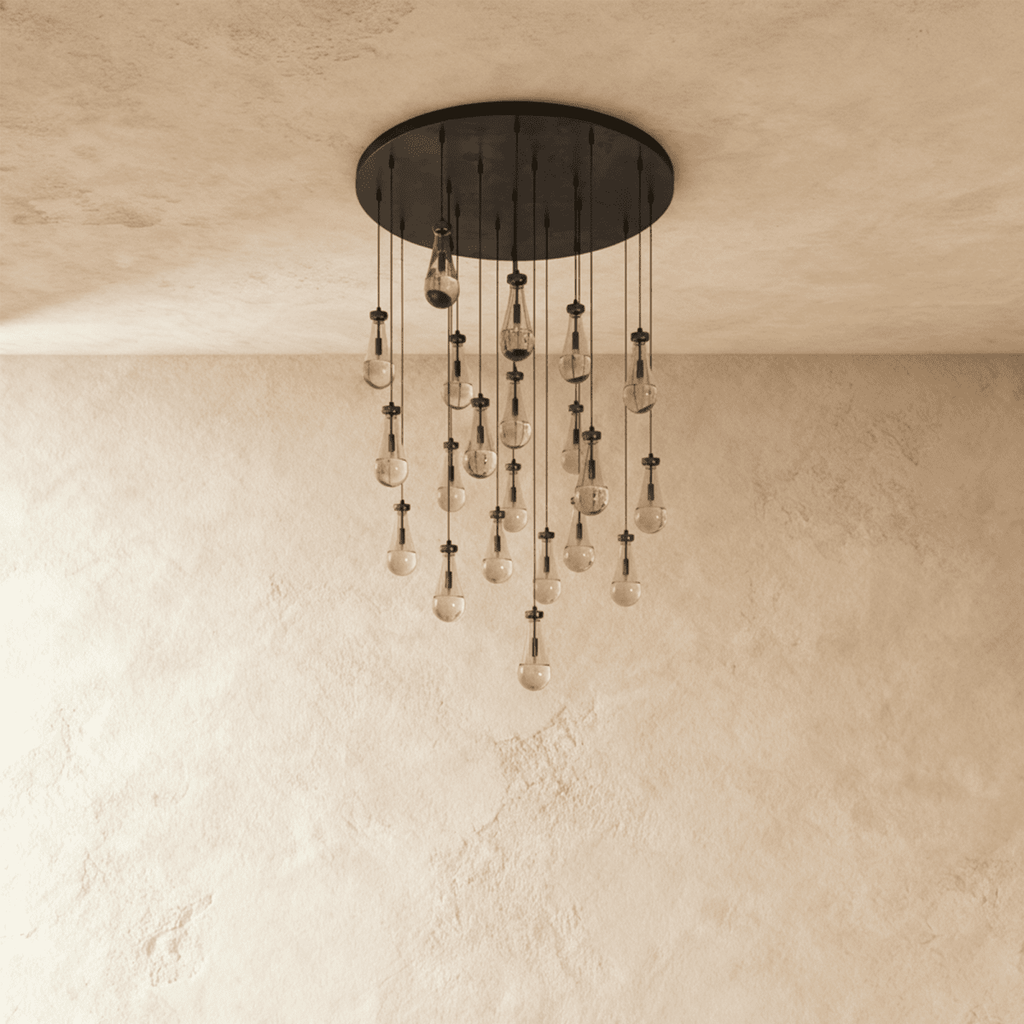 Clérachic chandelier with 21 clear glass teardrops on thin cords from a round dark bronze canopy, switched off, against limewashed plaster