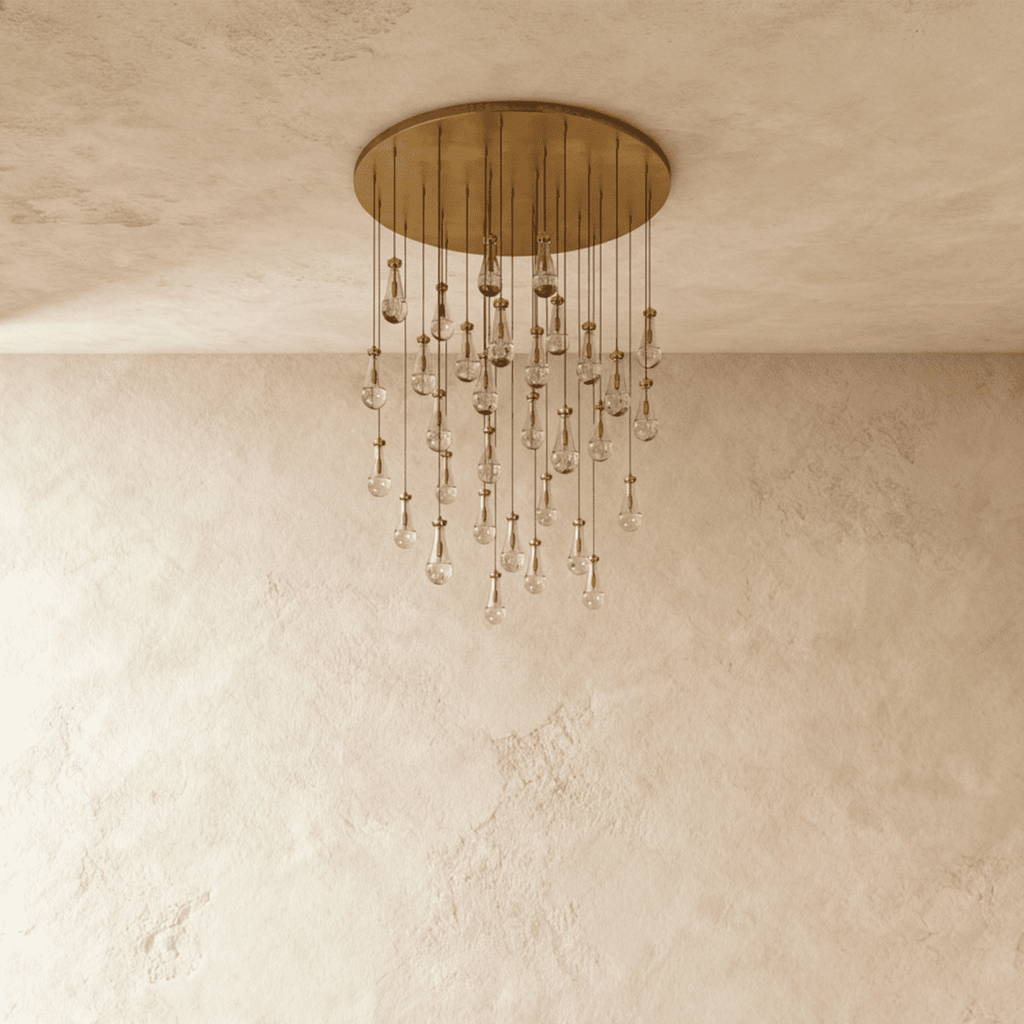 Clérachic chandelier with 31 clear glass teardrops on thin cords from a round brushed gold canopy, switched off, against limewashed plaster