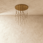 Clérachic chandelier with 31 clear glass teardrops on thin cords from a round brushed gold canopy, switched off, against limewashed plaster