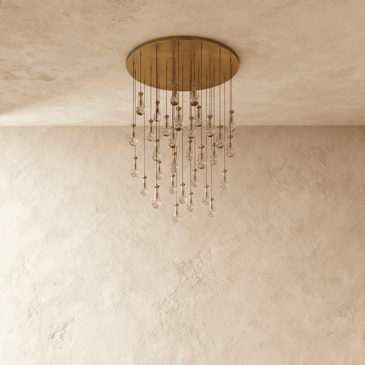 Clérachic chandelier with 31 clear glass teardrops on thin cords from a round brushed gold canopy, switched off, against limewashed plaster