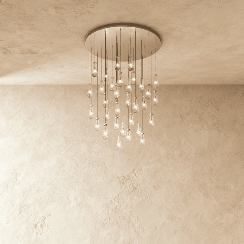 Clérachic chandelier with 31 clear glass teardrops on thin cords from a round satin nickel canopy, glowing warm, against limewashed plaster