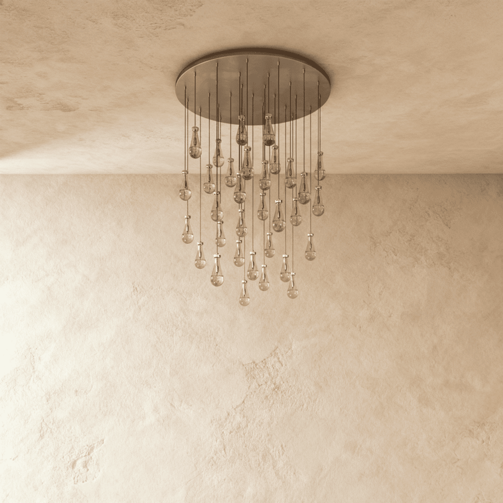 Clérachic chandelier with 31 clear glass teardrops on thin cords from a round satin nickel canopy, switched off, against limewashed plaster