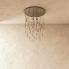 Clérachic chandelier with 31 clear glass teardrops on thin cords from a round satin nickel canopy, switched off, against limewashed plaster