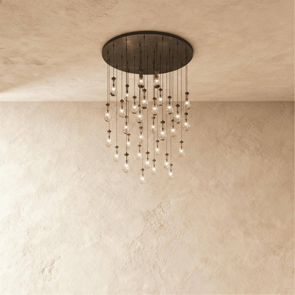 Clérachic chandelier with 31 clear glass teardrops on thin cords from a round dark bronze canopy, glowing warm, against limewashed plaster