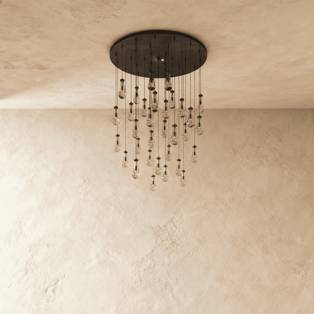Clérachic chandelier with 31 clear glass teardrops on thin cords from a round dark bronze canopy, switched off, against limewashed plaster