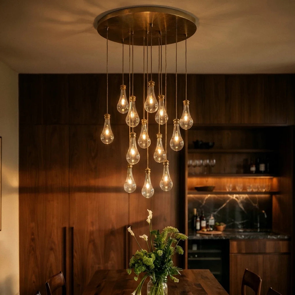 Clérachic chandelier in close view: clear glass bulbs on brass canopy, softly lit above a walnut dining room setting