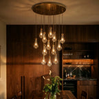 Clérachic chandelier in close view: clear glass bulbs on brass canopy, softly lit above a walnut dining room setting
