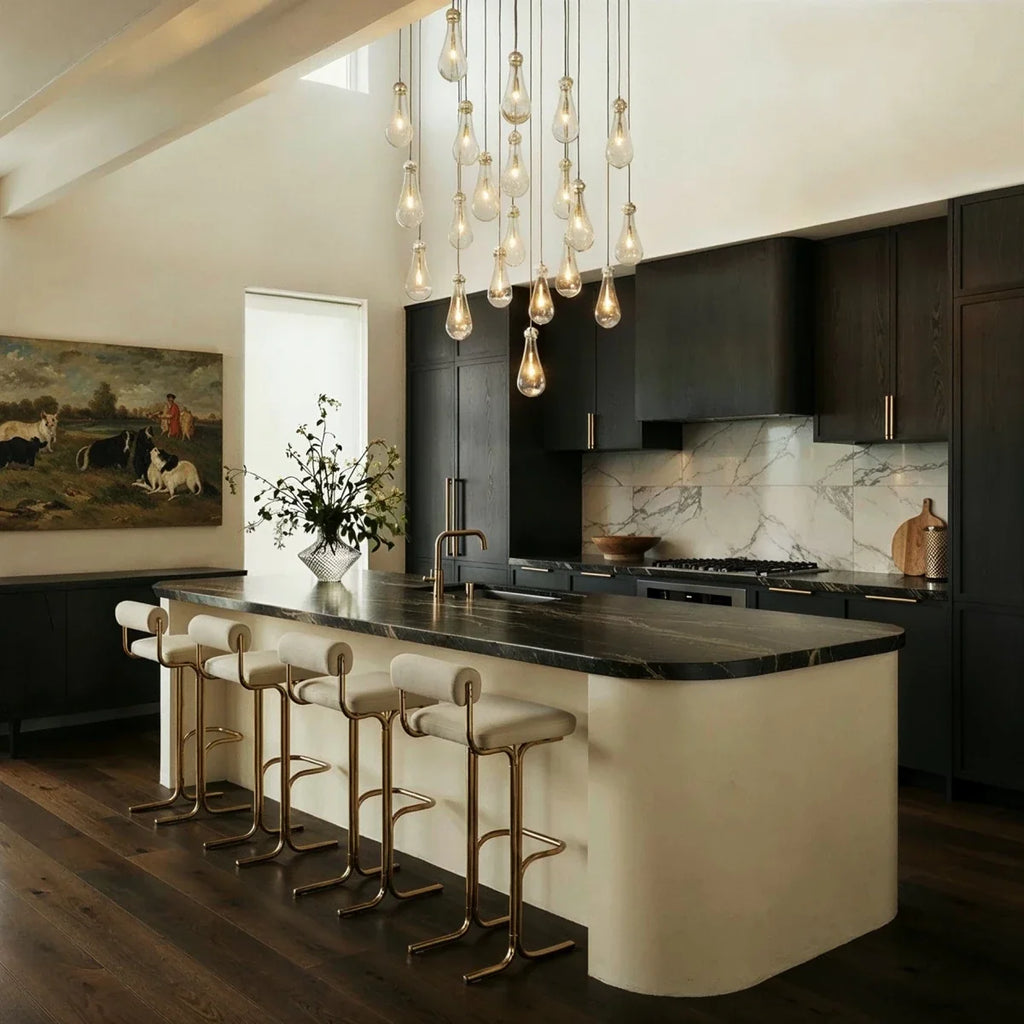 Clérachic cascade chandelier of clear glass drops hanging over a dark kitchen island with a marble top and brass stools