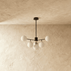 Clérachic black chandelier with 5 milky white glass globes on straight arms, unlit, against a limewash wall.