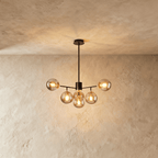 Clérachic black chandelier with 5 cognac glass globes on straight arms, lit warm, against a limewash wall.