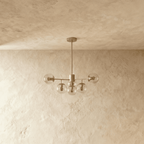 Clérachic gold chandelier with 5 pale cognac glass globes on straight arms, unlit, against a limewash wall.
