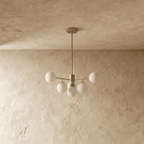 Clérachic gold chandelier with 5 milky white glass globes on straight arms, unlit, against a limewash wall.