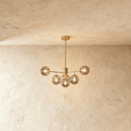 Clérachic gold chandelier with 5 smoky grey glass globes on straight arms, lit warm, against a limewash wall.