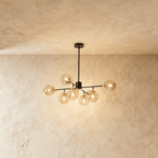 Clérachic black chandelier with 7 cognac glass globes on straight arms, lit warm, against a limewash wall.