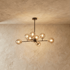 Clérachic black chandelier with 8 cognac glass globes on straight arms, lit warm, against a limewash wall.