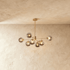Clérachic gold chandelier with 7 smoky grey glass globes on straight arms, lit warm, against a limewash wall.