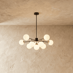 Clérachic black chandelier with 9 milky white glass globes on straight arms, lit warm, against a limewash wall.