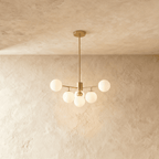 Clérachic gold chandelier with 5 milky white glass globes on straight arms, lit warm, against a limewash wall.