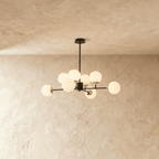 Clérachic black chandelier with 8 milky white glass globes on straight arms, unlit, against a limewash wall.