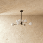 Clérachic black chandelier with 8 milky white glass globes on straight arms, unlit, against a limewash wall.