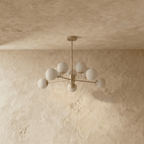 Clérachic gold chandelier with 9 milky white glass globes on straight arms, unlit, against a limewash wall.