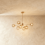 Clérachic gold chandelier with 7 cognac glass globes on straight arms, lit warm, against a limewash wall.