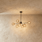 Clérachic black chandelier with 7 cognac glass globes on straight arms, lit warm, against a limewash wall.