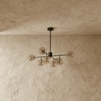 Clérachic black chandelier with 7 cognac-tinted glass globes on straight arms, unlit, against a limewash wall.