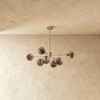Clérachic gold chandelier with 7 smoky grey glass globes on straight arms, unlit, against a limewash wall.